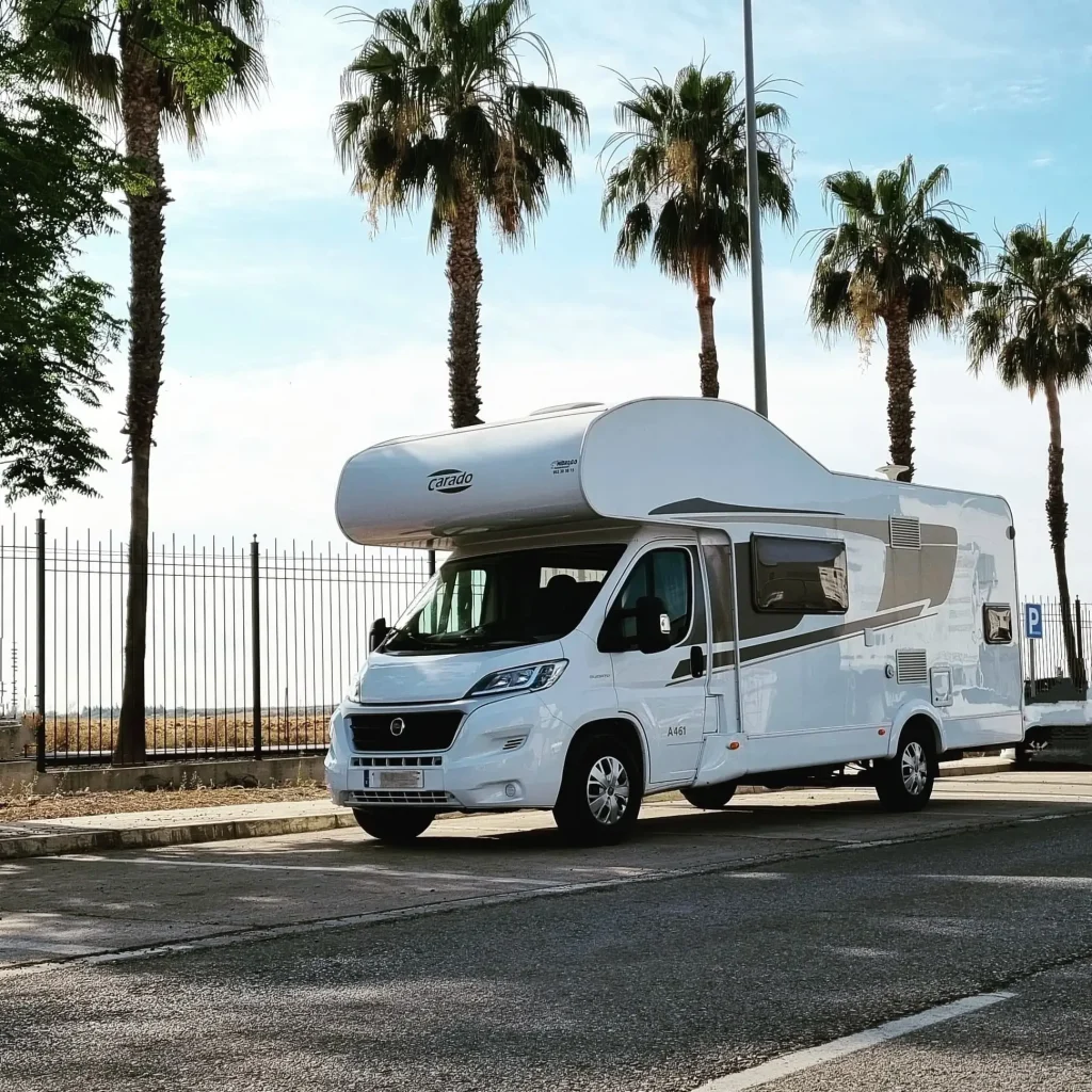 Autocaravana blanca estacionada bajo palmeras en una calle de Sevilla, ideal para disfrutar del alquiler de autocaravanas en Sevilla.