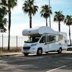 Autocaravana blanca estacionada bajo palmeras en una calle de Sevilla, ideal para disfrutar del alquiler de autocaravanas en Sevilla.