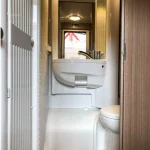 Baño completo de autocaravana con lavabo, espejo e inodoro, parte del equipamiento disponible en el alquiler de autocaravanas en Sevil