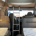 Interior de autocaravana con cama capuchina, vista desde la zona de comedor, ideal para ilustrar el alquiler de autocaravanas en Sevilla.