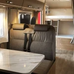 Interior de una autocaravana moderna con mesa, asientos cómodos y literas, ideal para disfrutar del alquiler de autocaravanas en Sevilla con total confort.
