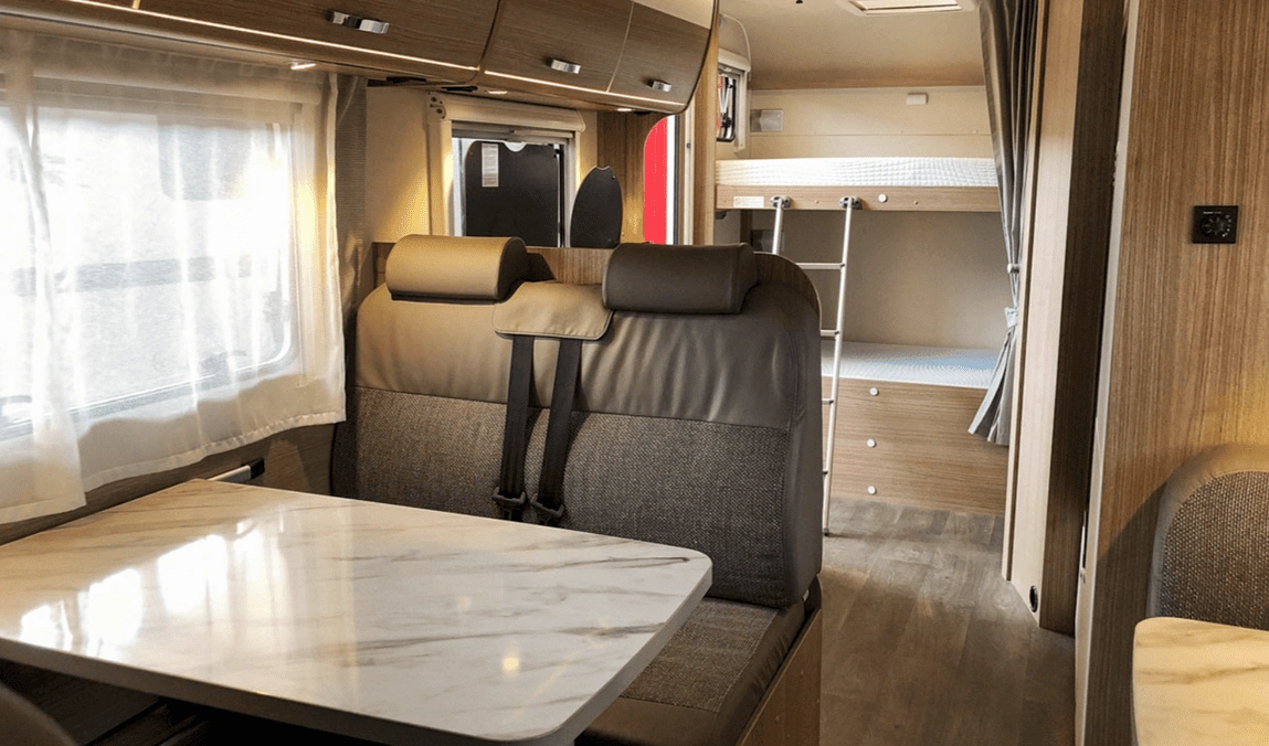 Interior de una autocaravana moderna con mesa, asientos cómodos y literas, ideal para disfrutar del alquiler de autocaravanas en Sevilla con total confort.